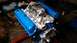 1977 Ford F-150 - A V8 engine assembly is shown with blue valve covers and a carburetor, resting on a red engine stand.