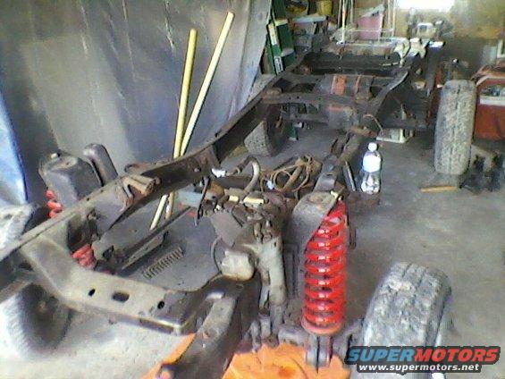 Truck frame with red springs and tires, in a garage
