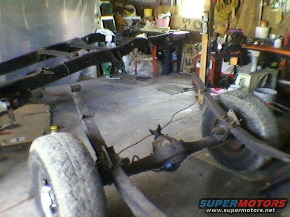 Truck frame with rear axle and leaf springs visible, in a garage setting