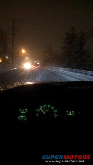 Dashboard gauges visible at night with snowy road ahead and oncoming headlights