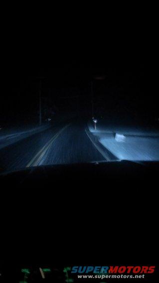 Dashboard view of a road at night with headlights illuminating the path