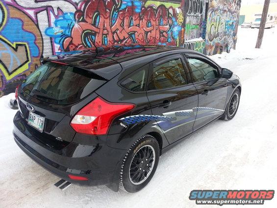 Black 2012 Ford Focus hatchback with custom decals parked on a snowy street next to graffiti-covered wall