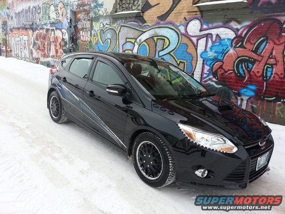 Black 2012 Ford Focus hatchback parked in snow with graffiti wall