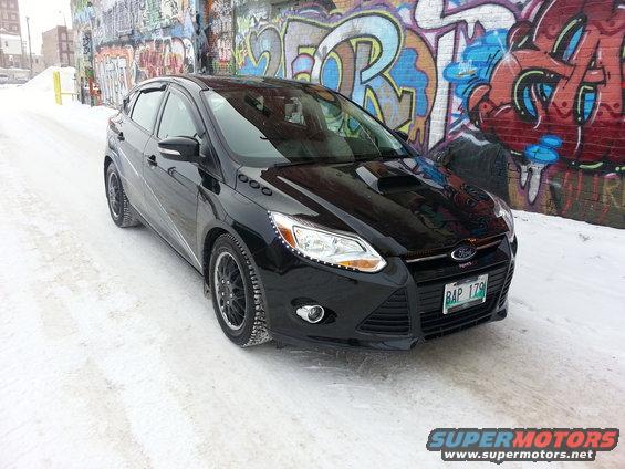 Black 2012 Ford Focus ST hatchback parked on a snowy street with graffiti wall behind it