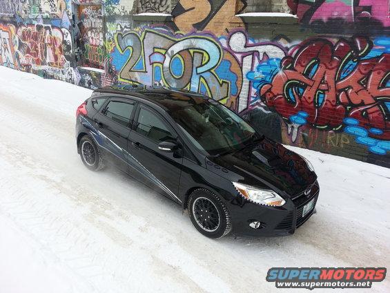 Black 2012 Ford Focus hatchback with aftermarket wheels parked on a snowy road