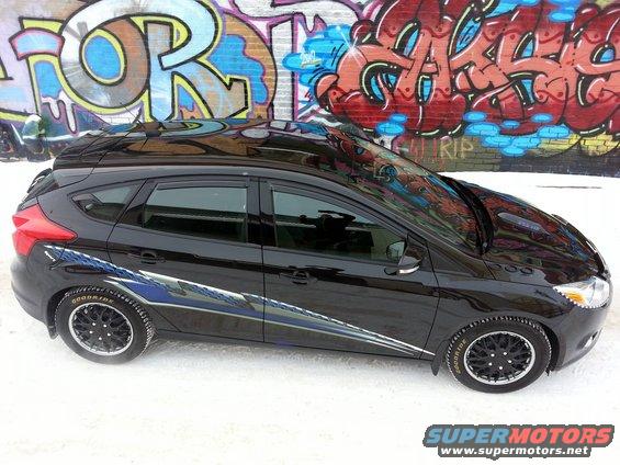 Black 2012 Ford Focus hatchback with racing stripes parked in front of graffiti