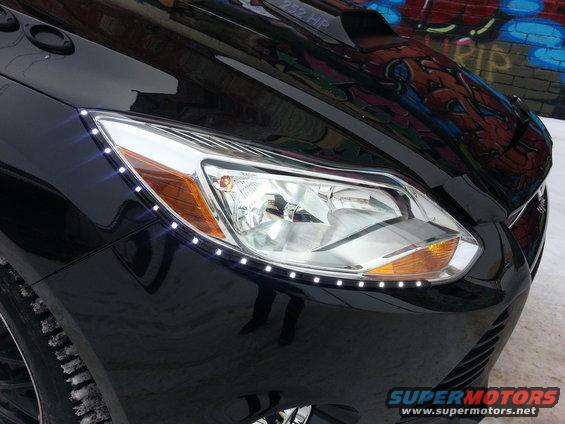 Black car front end with LED strip lights along the headlight, snow on the ground