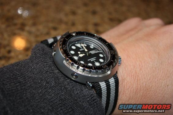 Dive watch with black dial and striped NATO strap on a wrist