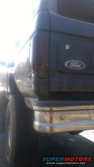 Dark SUV's rear quarter panel with a chrome bumper and Ford emblem. The taillight is tinted