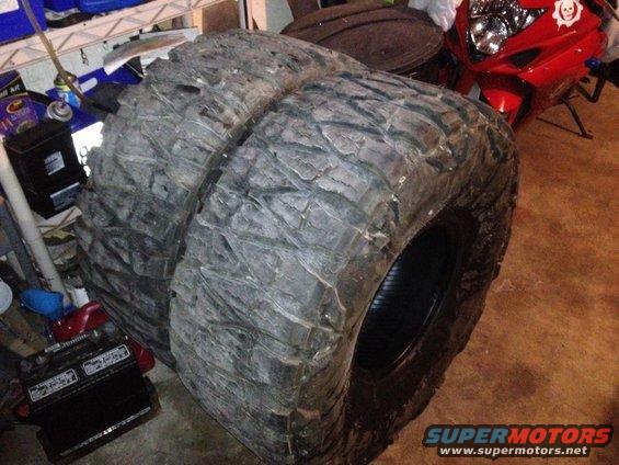 Two large, knobby off-road tires stacked in a garage. A red motorcycle is visible in the background