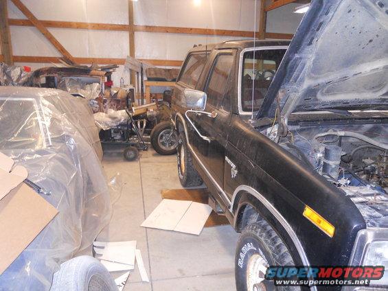 Black Ford Bronco in garage with hood up, another car covered in plastic to the left