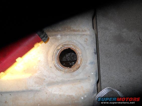 Close-up of a rusty fuel tank opening with some liquid visible inside