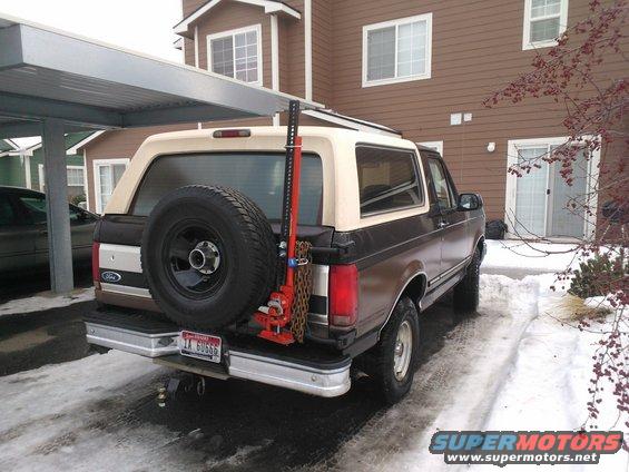 Rear view of a brown and tan 1992 Ford Bronco with a spare tire and a red Hi-Lift jack mounted on the back