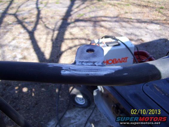 Welding bracket on a dark metal tube with a Hobart welder in the background