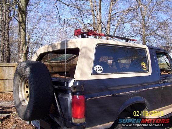 Dark blue 1990 Ford Bronco with tan soft top, spare tire on rear, and hi-lift jack mounted on roof rack