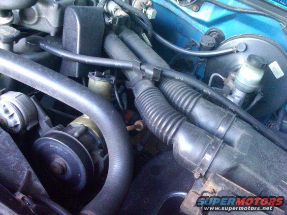 Engine bay of a 1993 Ford Bronco with blue paint, showing hoses, belts, and a brake booster