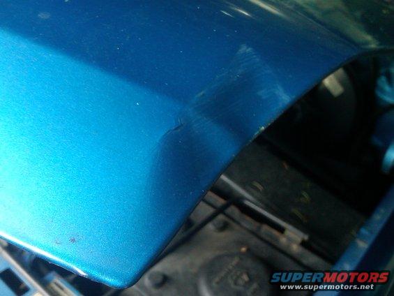 Close-up of blue fender with minor scratches and a small dent