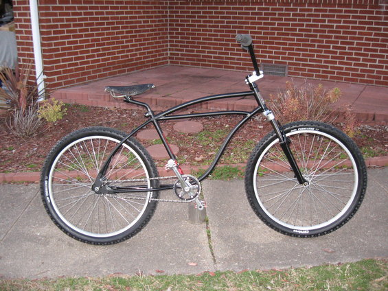 Black custom cruiser bicycle with wide tires and a curved frame, parked on a sidewalk