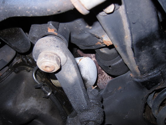 Close-up of a car's suspension system, showing a greasy metal part and part of an oil filter