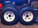 1994 Ford Bronco - Four tires with white rims are stacked in a garage setting.