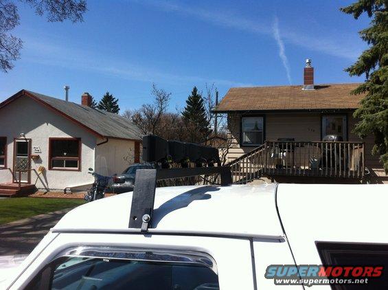 White SUV roof with a black rack holding a dark object, houses and trees in background
