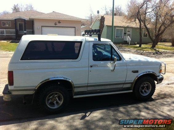 White 1994 Ford Bronco parked on street, side view. Has roof rack with lights