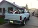 1994 Ford Bronco - A white pickup truck carries a dirt bike in its bed, with a motorcycle and a person visible near a garage.