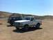 1994 Ford Bronco - Two SUVs, a white Ford Bronco and a black one, are parked in a dirt area with hills in the background.