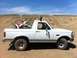 1994 Ford Bronco - A white Ford Bronco carries a dirt bike in its bed, parked on a dirt lot with a hill and blue sky overhead.