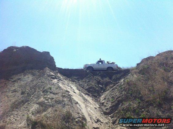 White pickup truck with dirt bike in bed on top of a steep dirt embankment under a clear blue sky