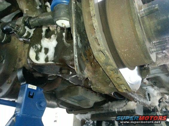 close-up of rusty brake rotor and suspension components on a vehicle supported by a blue jack