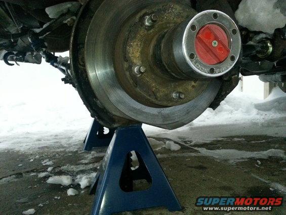 Vehicle wheel hub with red locking mechanism on jack stands in snow