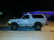 1994 Ford Bronco - A white 1994 Ford Bronco is parked on a snowy street at night, with house lights and blue Christmas lights visible in the background.