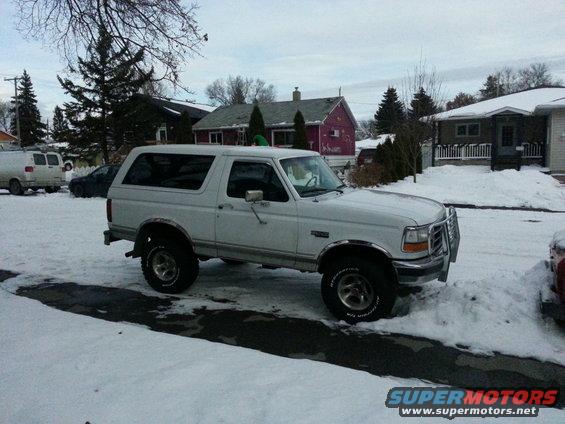 White Ford Bronco parked in snow, 3/4 front view. Chrome grille guard and fender trim visible