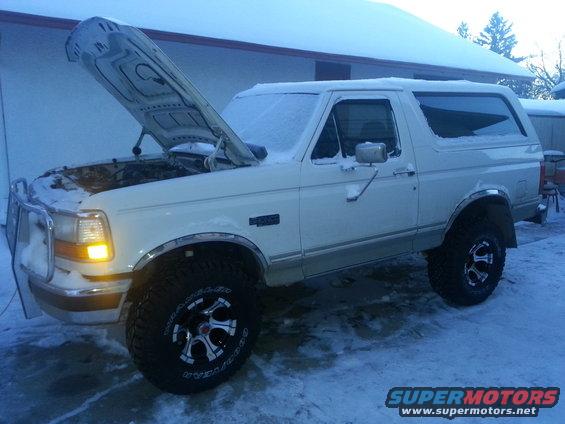 White Ford Bronco parked outside in the snow with hood open, showing engine bay. Aftermarket wheels are visible
