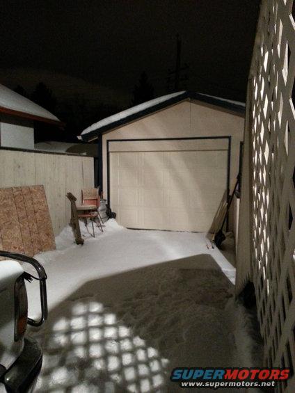 Vehicle rear corner in snow, with garage and fence