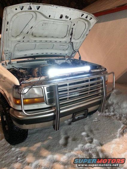 White Ford truck front end, hood open, with a light bar illuminating the engine bay. Snow on the ground