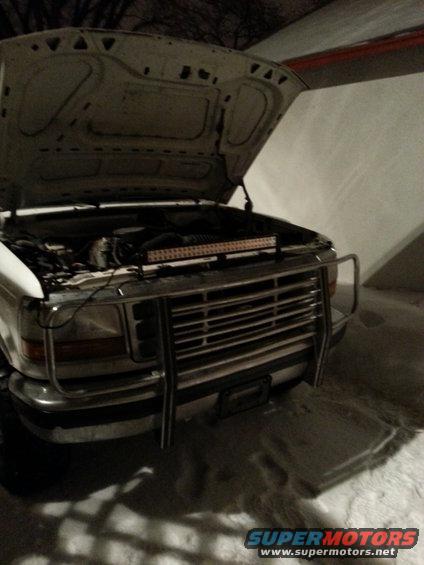 White pickup truck with hood up, showing engine and a light bar across the front