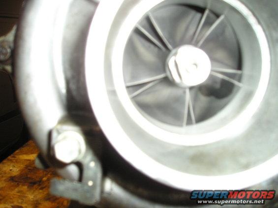 Close-up of a turbocharger's compressor wheel and housing. A "SUPERMOTORS" watermark is visible