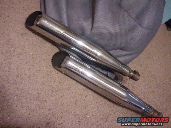 Two chrome motorcycle exhaust pipes lying on a carpeted floor