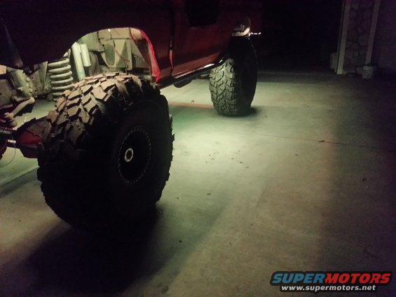 Modified off-road vehicle with large tires and visible suspension components, illuminated by underglow lights