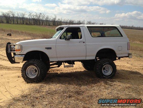 White lifted SUV with large tires parked on dirt. Has a brush guard on the front