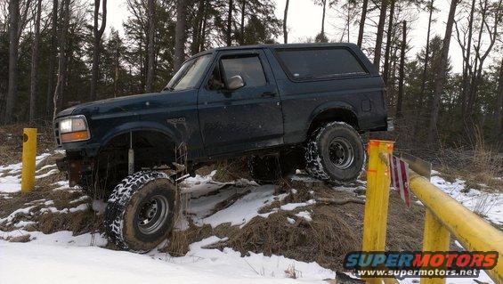 1995 Ford Bronco driving over snowy terrain with trees in the background