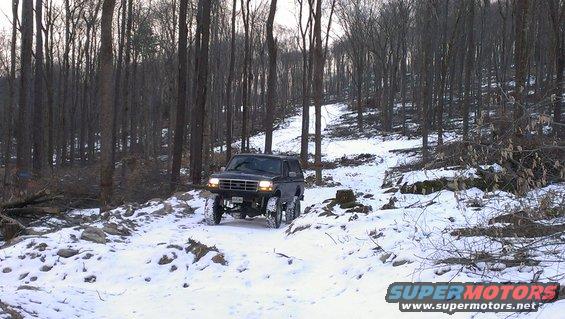1995 Ford Bronco driving on a snowy forest road with trees on either side