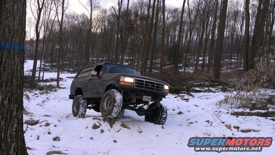 Ford Bronco driving on a snowy trail in the woods. It has large off-road tires and a lifted suspension