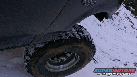 Dark Ford Bronco tire on snowy incline, "BRONCO" badge visible