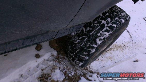 Close-up of a vehicle's tire partially buried in snow and mud