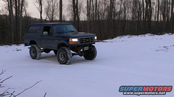 Dark SUV with lifted suspension driving in snow, front grille visible