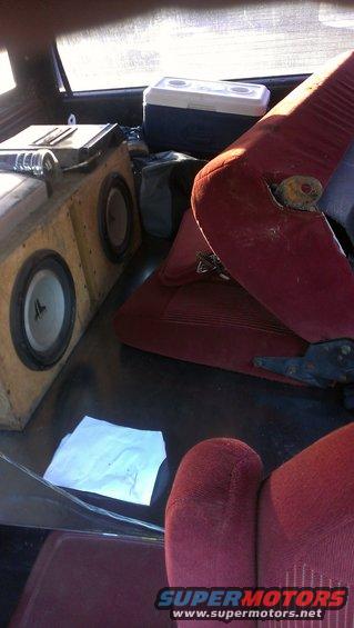 Interior shot of a vehicle showing red seats, a cooler, and a large wooden box with two speakers