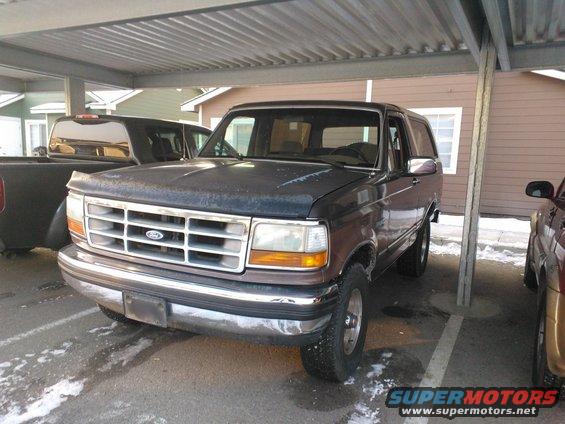 1992 Ford Bronco parked under a carport with another truck to the left and a vehicle to the right